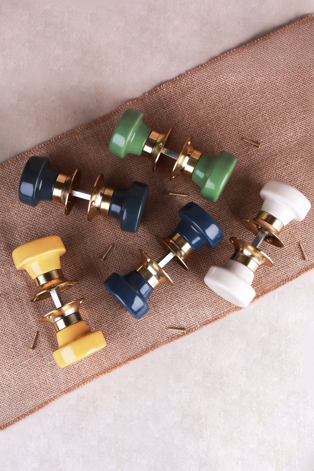 Five ceramic mortice door knob sets joined on their spindles, in charcoal, sage green, navy blue, cream and yellow, on a linen runner