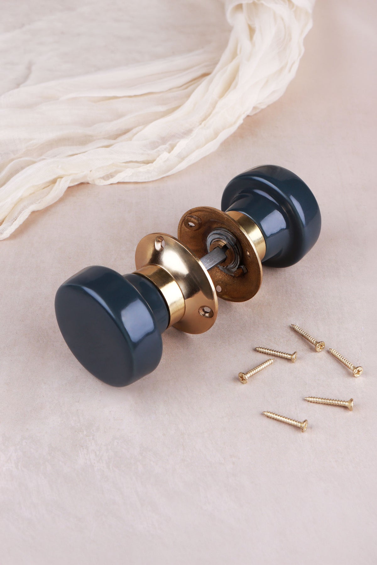 Charcoal ceramic mortice door knobs joined by the spindle through their polished brass roses, as they sit on a door