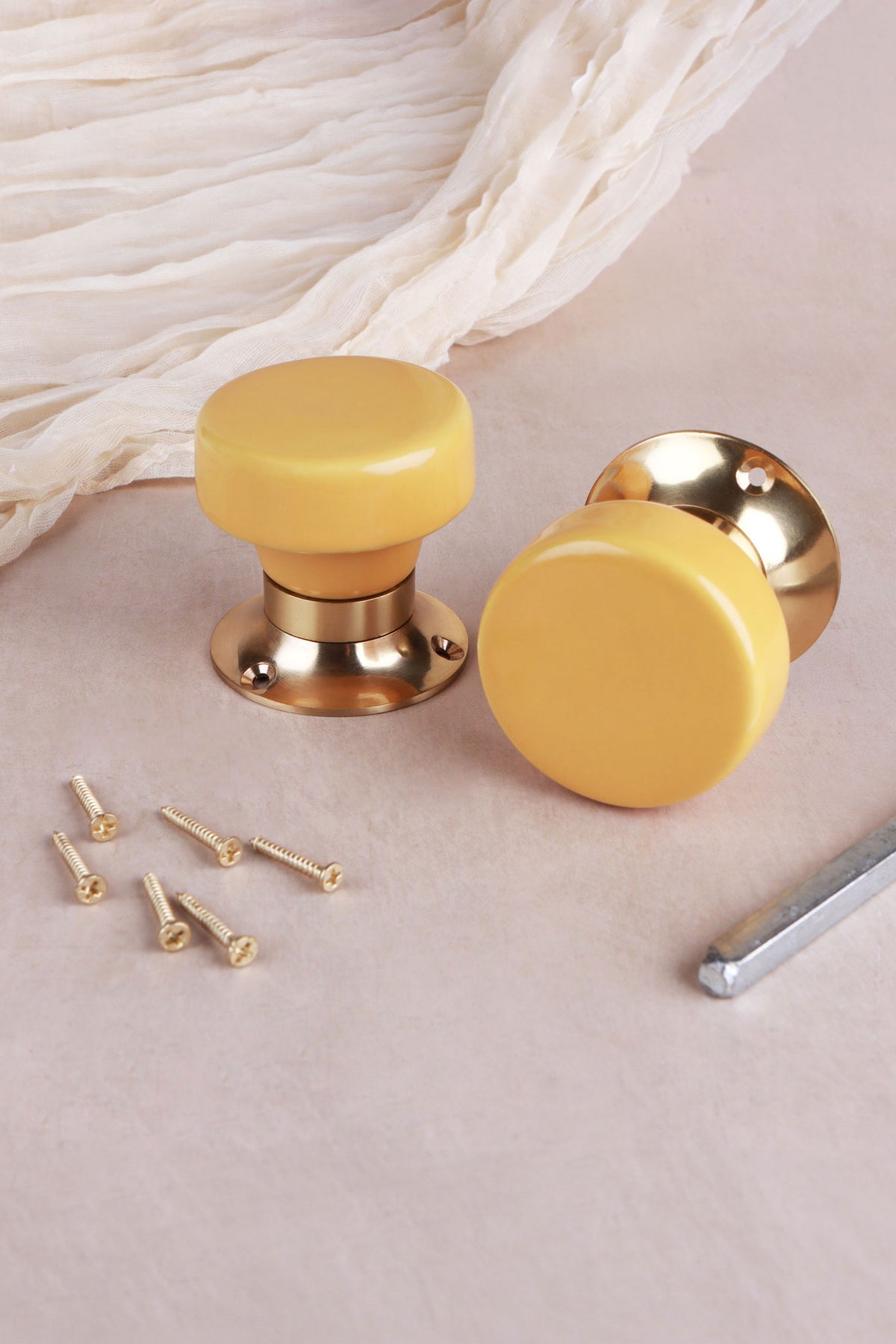 Yellow ceramic door knob standing on its polished brass rose beside the second knob, with the spindle and fixing screws