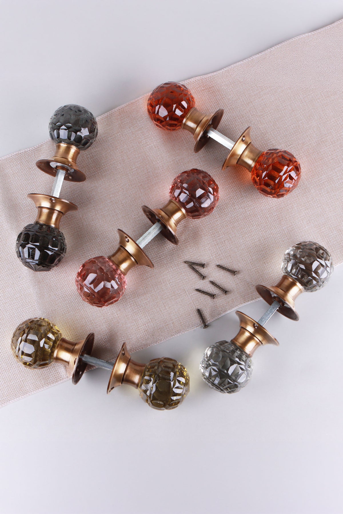 Five pairs of faceted glass mortice door knobs joined on their spindles, in smokey grey, amber, blush pink, ivory and clear crystal