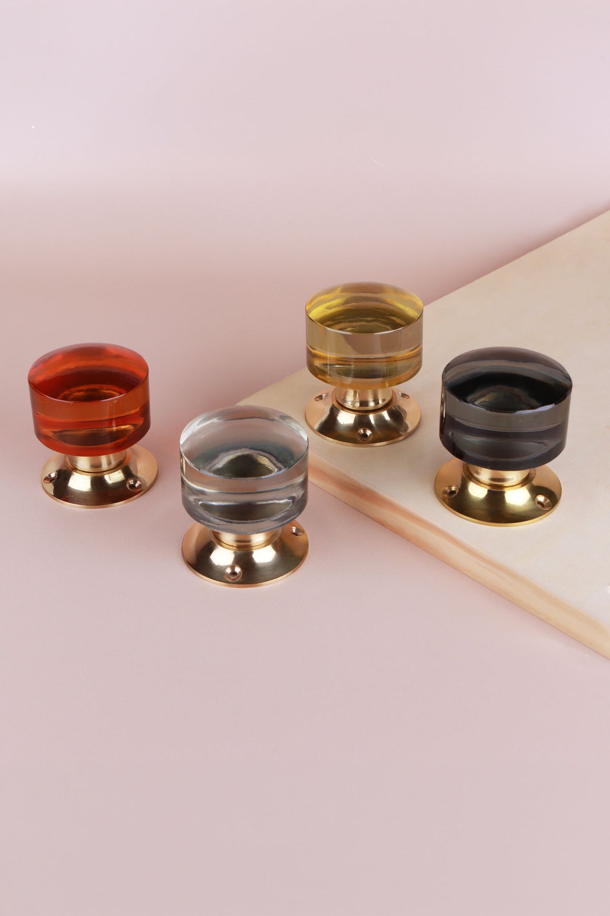 Four cylinder glass door knobs on polished brass roses in amber, clear crystal, ivory and smokey grey, beside a wooden board