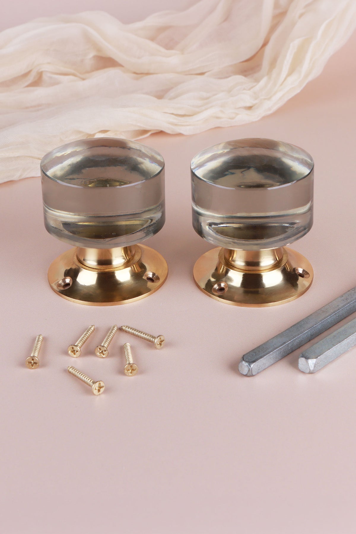 Two clear glass cylinder door knobs standing on their polished brass roses, with the square spindles and fixing screws