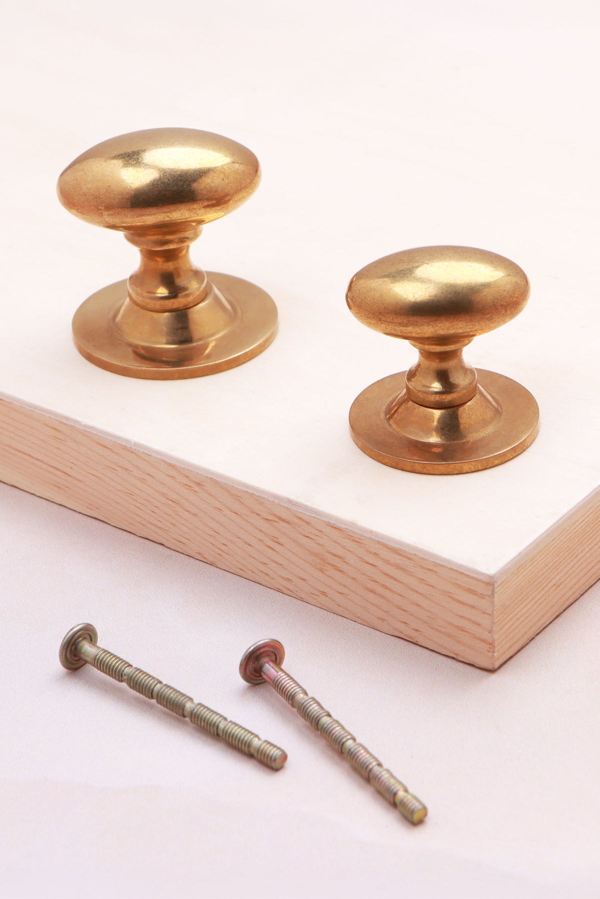 Aged brass oval knobs on roses, 32mm and 38mm, with fixing bolts