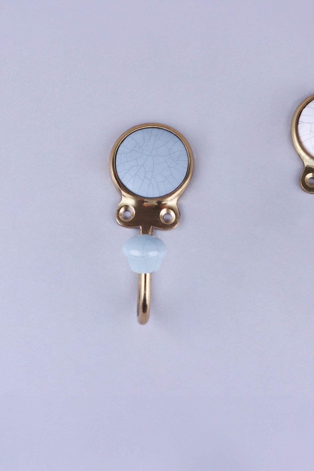 Blue-grey crackle glaze ceramic coat hook: pale blue-grey disc with fine crackle lines in a gold-tone frame, with a pale blue knob