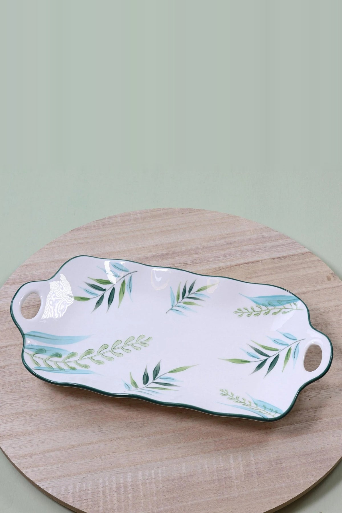 Long white ceramic serving platter with green and blue leaf sprays, a green rim and cut-out handles at each end