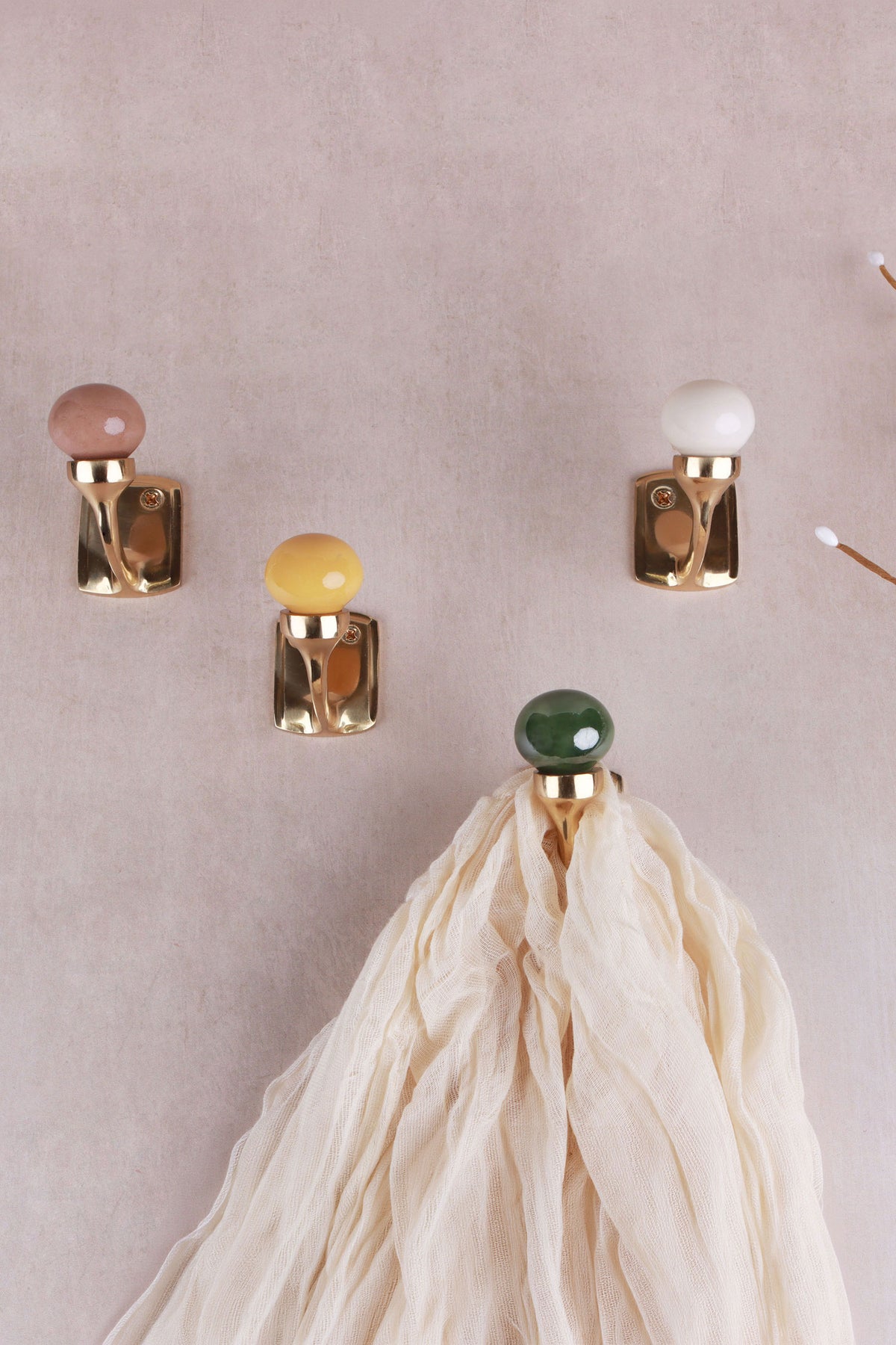 Ceramic ball hooks in rosy brown, cream, mustard yellow and green on a pale pink wall, a cream scarf hanging from the green hook