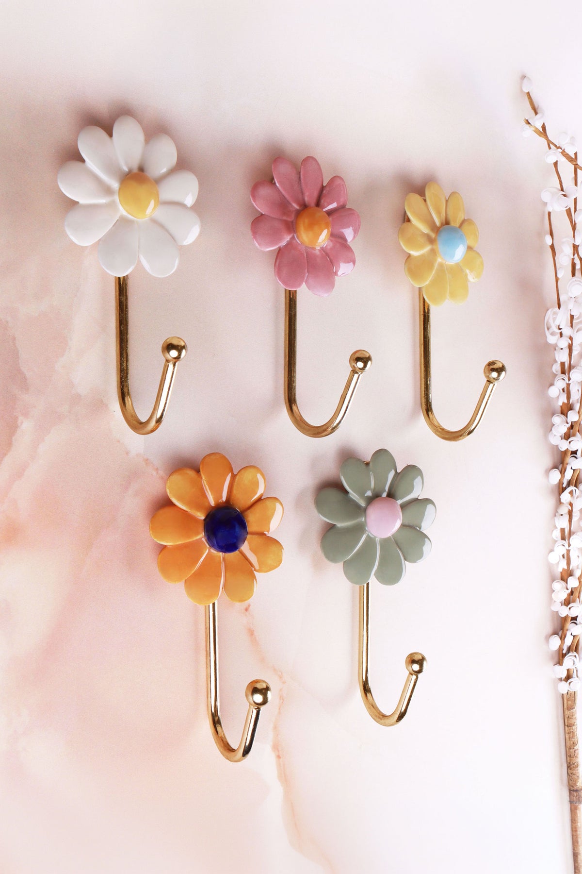 Five ceramic daisy wall hooks on a pink marble background: white, pink and yellow on top, dark yellow and sage green below