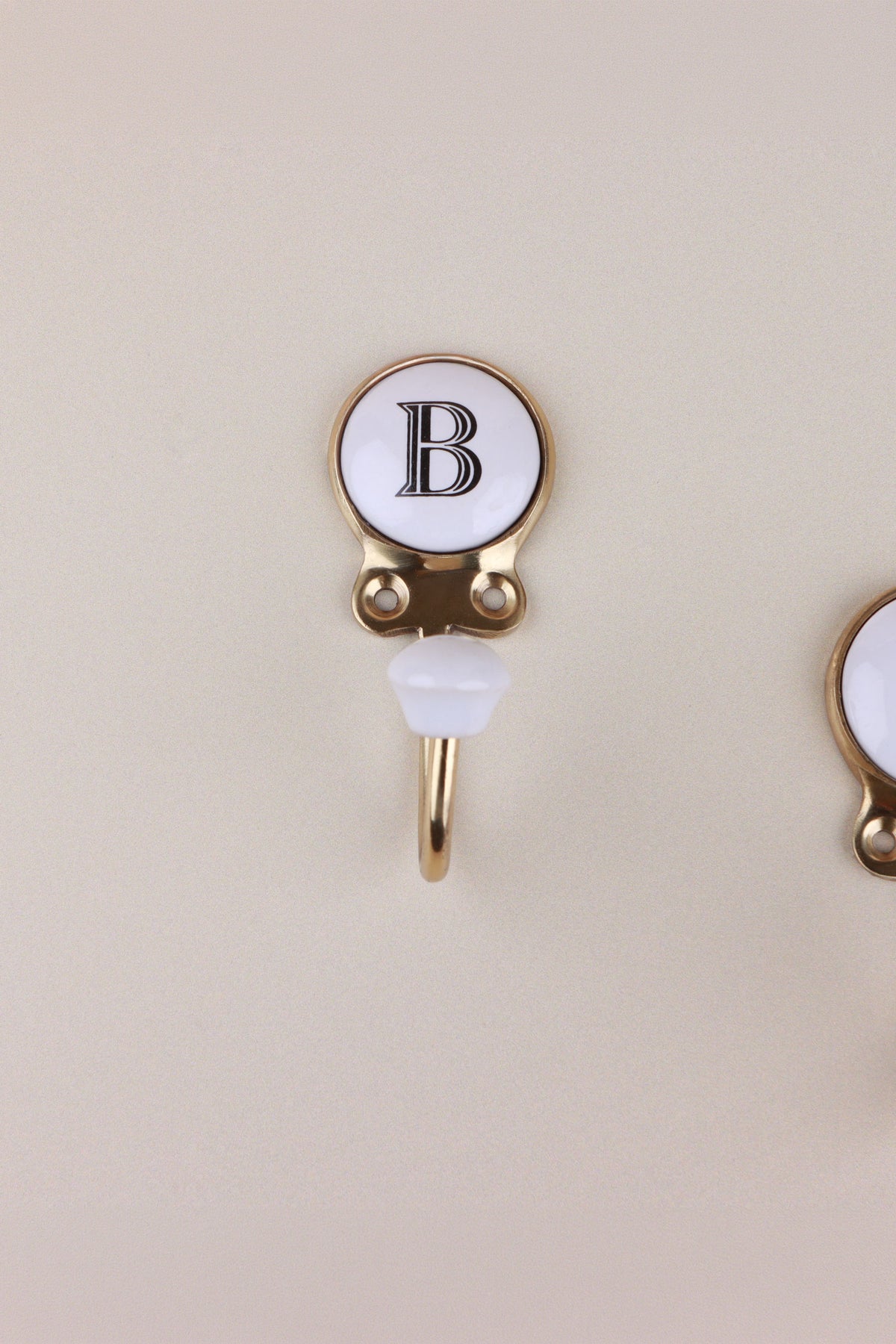Letter B ceramic hook: white disc with a black serif capital B in a gold-tone frame, with a white ceramic knob