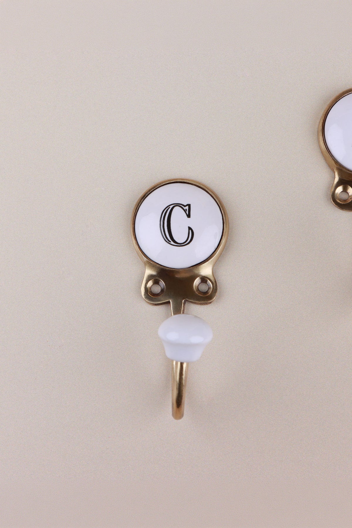 Letter C ceramic hook: white disc with a black serif capital C in a gold-tone frame, with a white ceramic knob