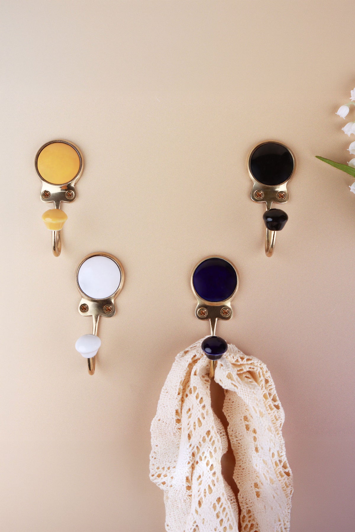 Ceramic coat hooks in yellow, black, white and dark blue, each with a matching ceramic knob, a lace cloth hanging from the dark blue hook