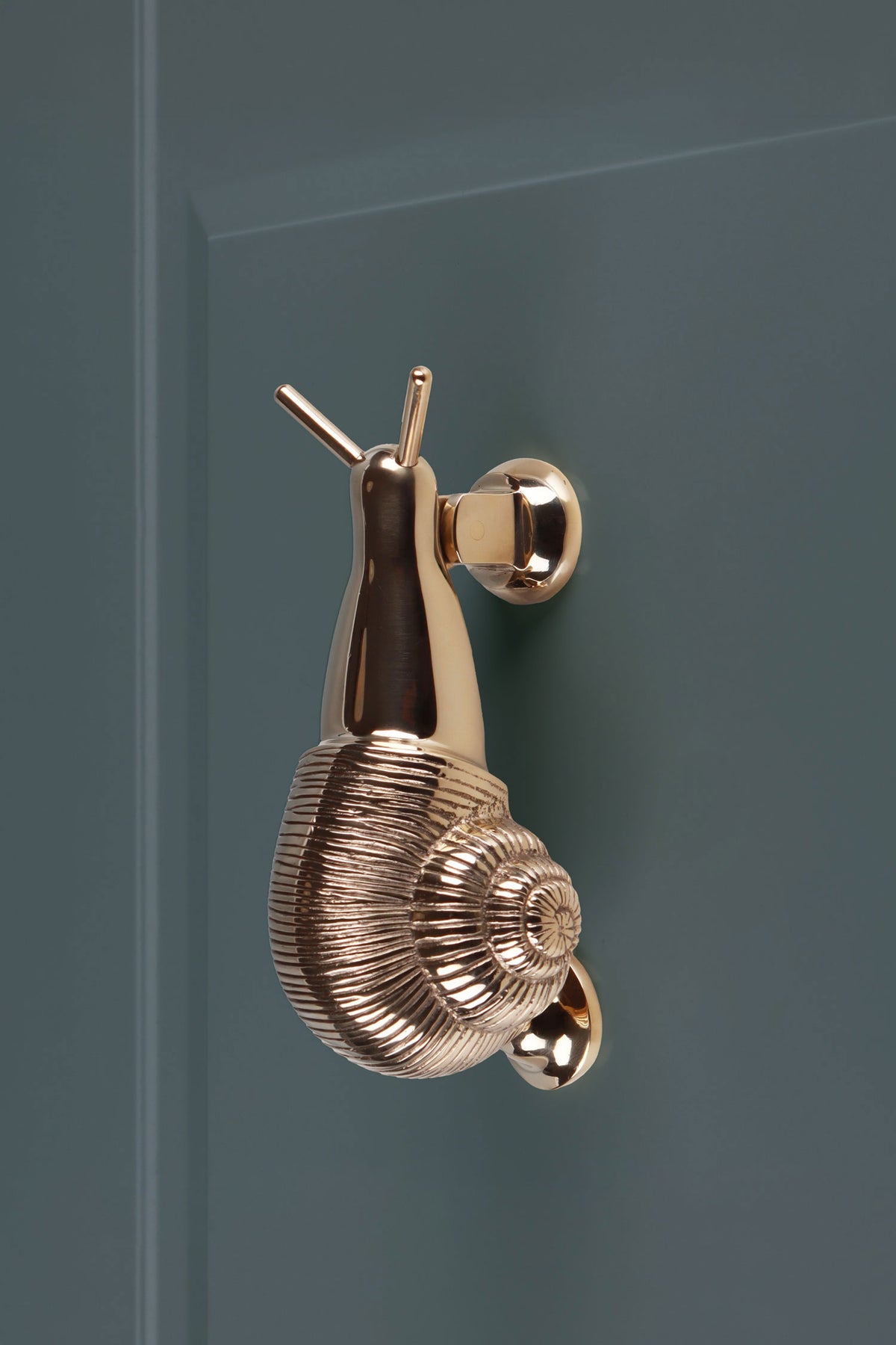 Polished brass snail door knocker fitted to a teal front door, with its round strike button below