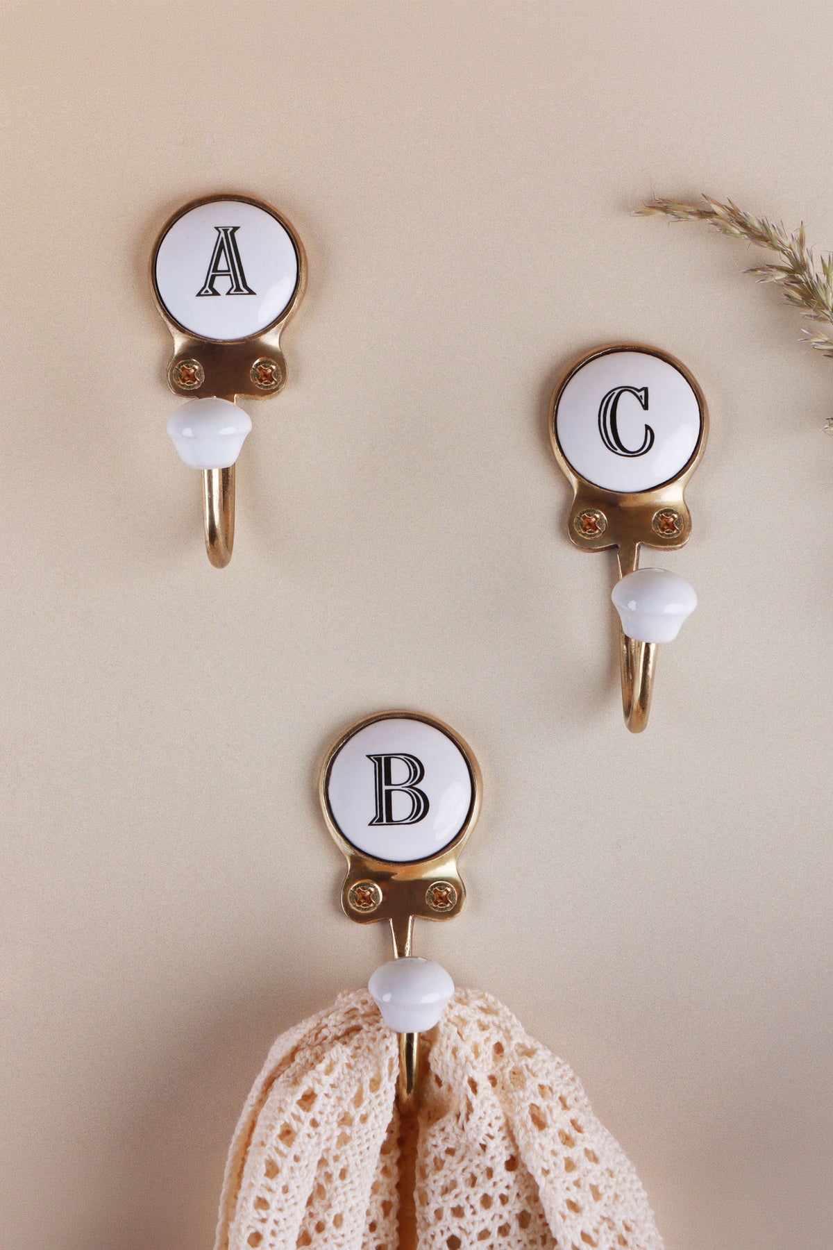 Three ceramic letter wall hooks, A, C and B, with a crochet lace cloth hanging from the B hook