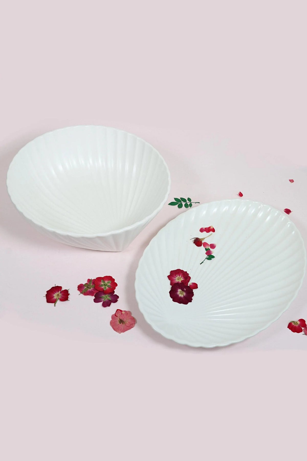 White porcelain shell serving bowl and oval shell dish on a pale pink surface scattered with small red flowers