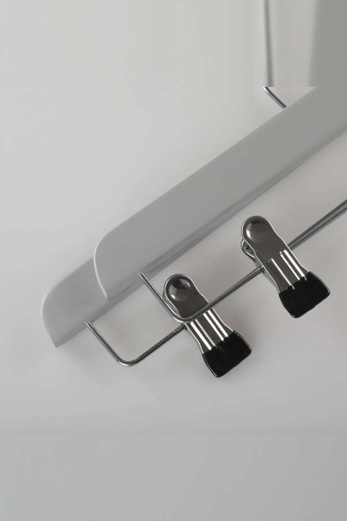 Close-up of a grey wooden clip hanger showing the two metal clips with black tips