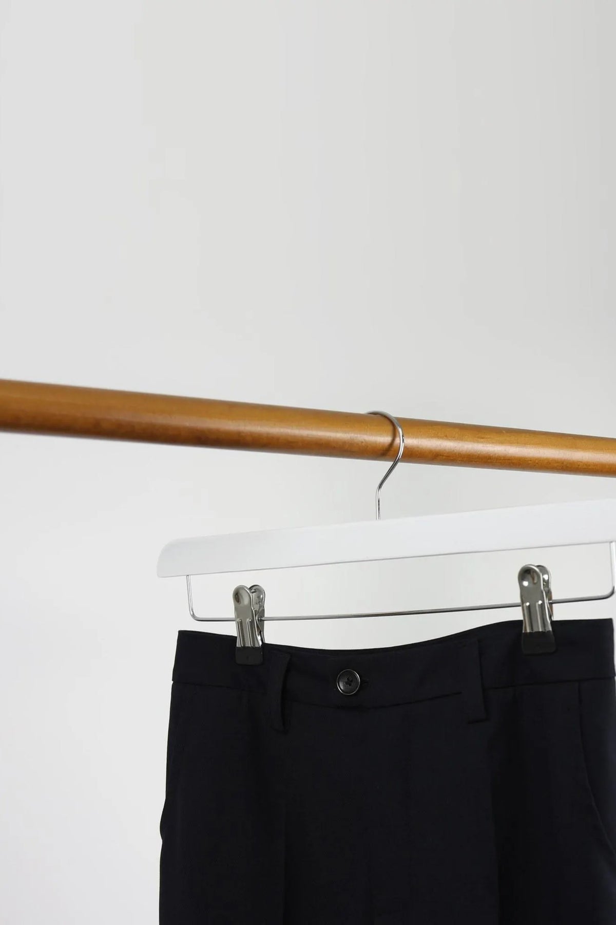 White wooden clip hanger holding black trousers on a wooden rail