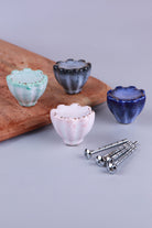 Four fluted ceramic cabinet knobs in turquoise, black, pink and blue with gold-coloured dots on the scalloped rims, beside their M4 bolts