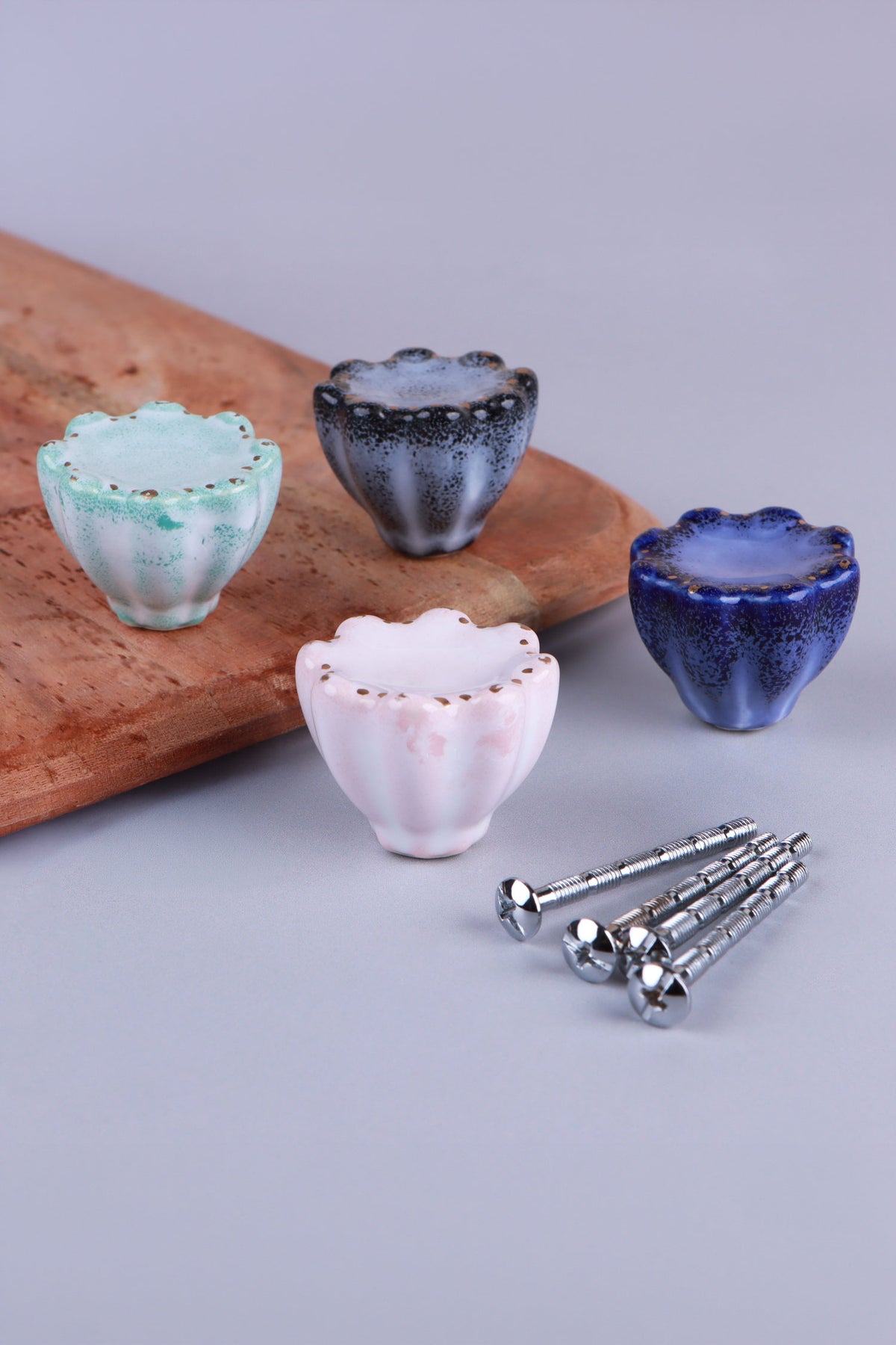 Four fluted ceramic cabinet knobs in turquoise, black, pink and blue with gold-coloured dots on the scalloped rims, beside their M4 bolts