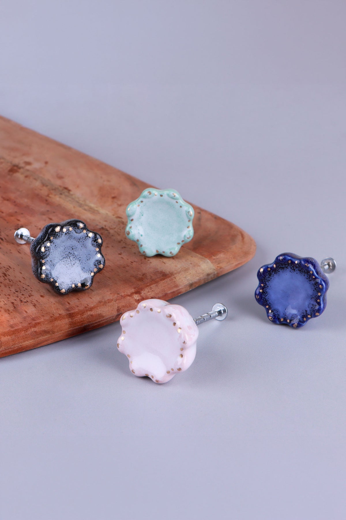 Top view of four scalloped ceramic knobs in black, turquoise, pink and blue, showing the speckled glaze and gold-coloured dots