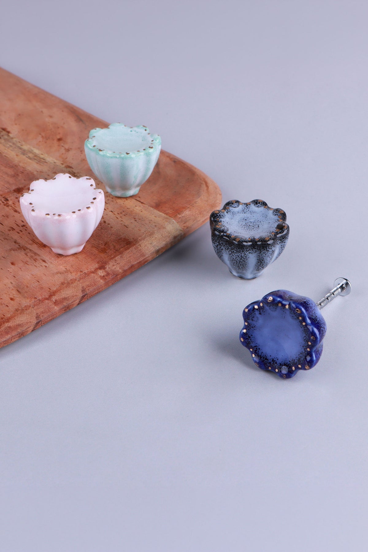 Four scalloped ceramic drawer knobs in pink, turquoise, black and blue on a wooden board, the blue knob with its M4 bolt fitted