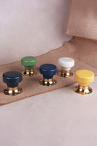 Five flat ceramic door knobs on polished brass roses in a row: charcoal, sage green, navy blue, cream and yellow