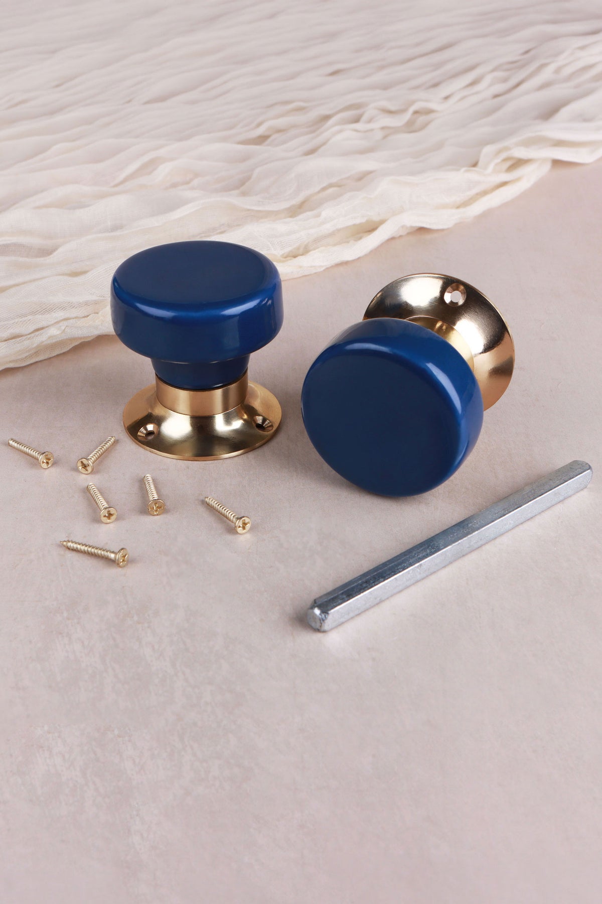 Navy blue ceramic door knob standing on its polished brass rose beside the second knob, with the spindle and fixing screws
