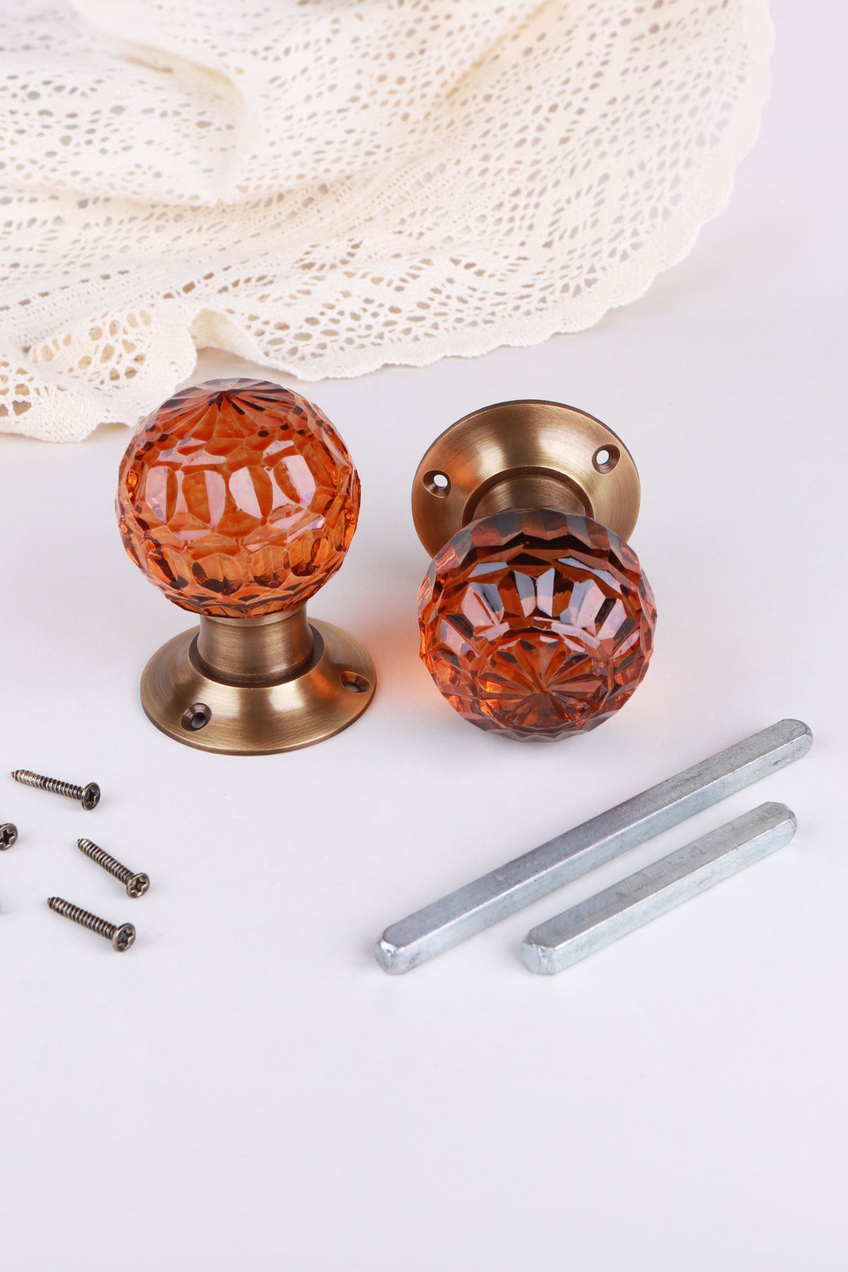 Amber faceted glass door knob standing on its antique brass rose beside the second knob lying on its side, with the spindles and screws