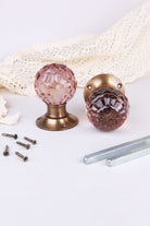 Blush Pink faceted glass door knob standing on its antique brass rose beside the second knob lying on its side, with the spindles and screws