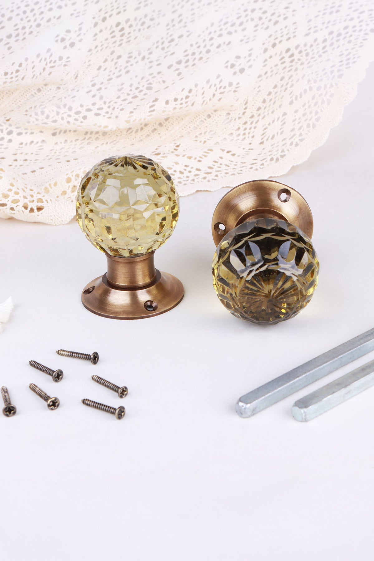 Ivory faceted glass door knob standing on its antique brass rose beside the second knob lying on its side, with the spindles and screws