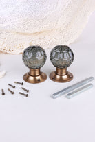 Pair of smokey grey faceted glass mortice door knobs on antique brass roses, with the square spindles and fixing screws