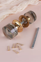 Clear glass cylinder mortice door knobs joined by the spindle through their polished brass roses, as they sit on a door