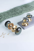 Dome glass mortice door knobs on polished brass roses: a clear crystal pair standing on a grey board and a smokey grey pair joined on its spindle, with fixing screws