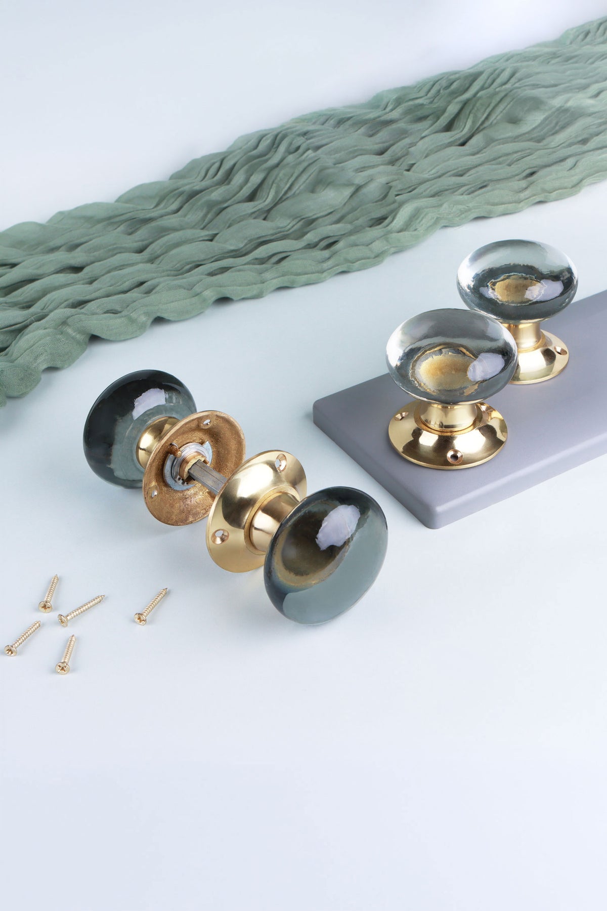 Dome glass mortice door knobs on polished brass roses: a clear crystal pair standing on a grey board and a smokey grey pair joined on its spindle, with fixing screws