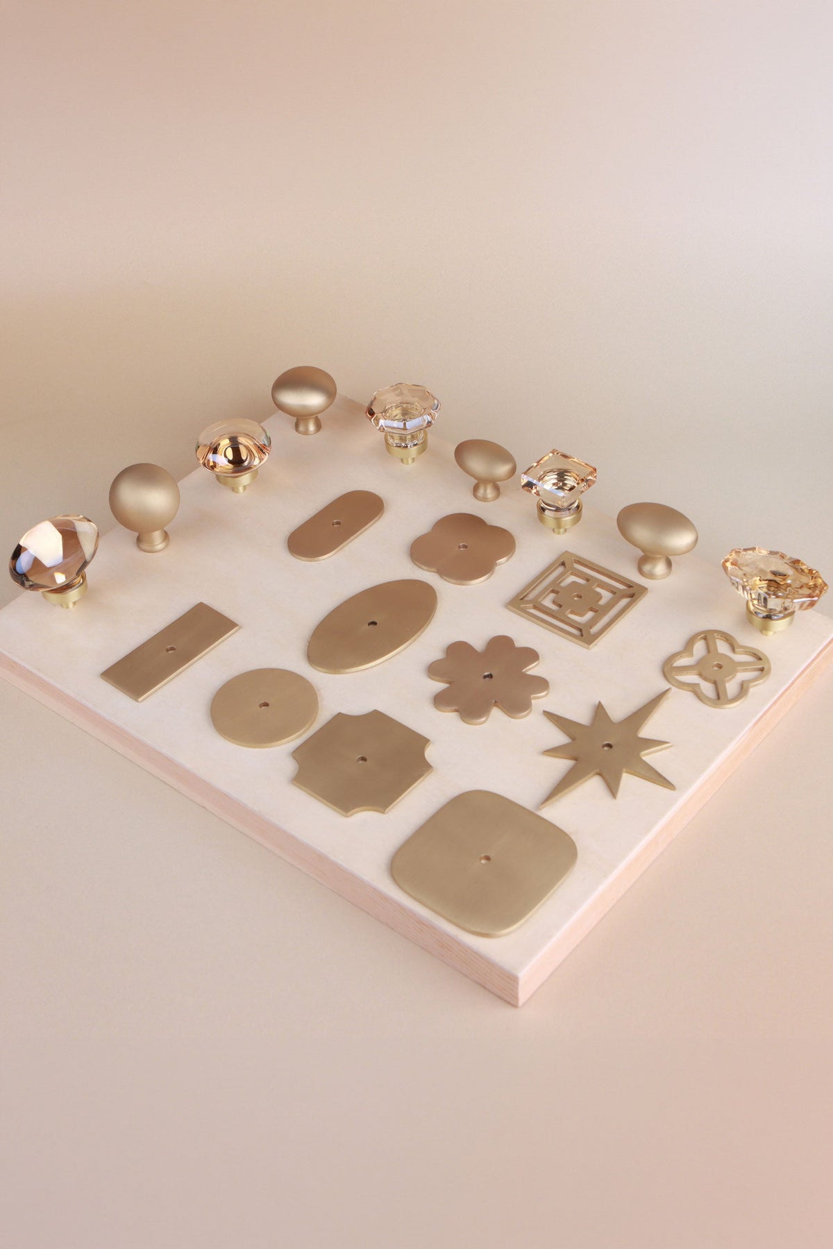 Champagne crystal knobs and eleven satin brass backplate shapes laid out on a board