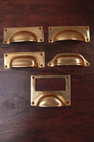 Five aged brass cup pull shapes — bevelled plate, square plate, rounded plate, deep scoop and card frame