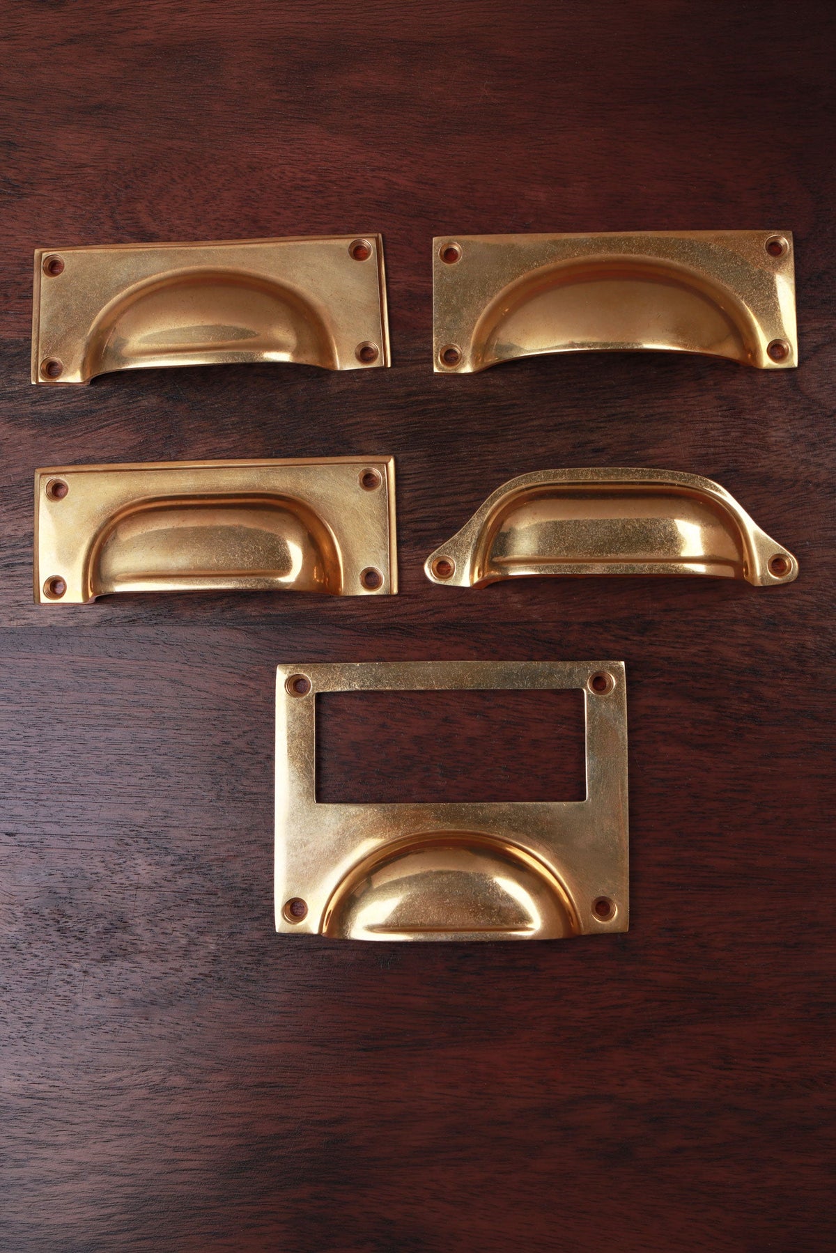 Five aged brass cup pull shapes — bevelled plate, square plate, rounded plate, deep scoop and card frame