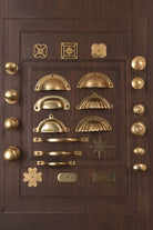 Aged brass cabinet knobs, cup pulls, D handles and backplates laid out on a panelled cupboard door