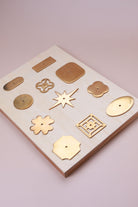 Eleven aged brass cabinet knob backplates on a pale wooden board: round, oval, square, squircle, quatrefoil, pierced, fretwork, flower, star, oblong and rectangle