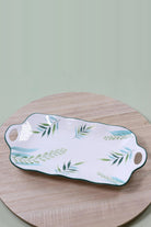 Long white ceramic serving platter with green and blue leaf sprays, a green rim and cut-out handles at each end