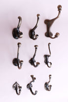 Nine cast iron coat hooks in an antique brass finish on a pale pink wall, from small single hooks to a large hat and coat hook
