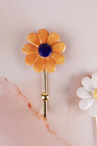 Dark yellow ceramic daisy wall hook with deep marigold petals and a navy blue centre on a gold-tone metal hook