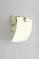 Gold toilet roll holder with a curved cover, seen from the side, on a white Greek key wall plate