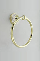Gold towel ring on a round white wall plate with a gold Greek key border, on a grey tiled wall