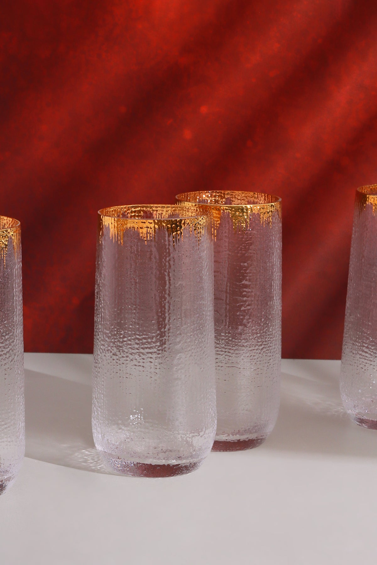Hammered glass tumblers with gold rims on a white table against a red wall