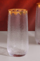 Close-up of a hammered glass tumbler with a gold rim against a red background