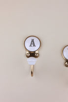 Letter A ceramic hook: white disc with a black serif capital A in a gold-tone frame, with a white ceramic knob