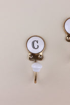 Letter C ceramic hook: white disc with a black serif capital C in a gold-tone frame, with a white ceramic knob