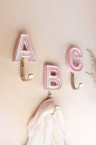Pink ceramic letter wall hooks with gold rims on gold-tone hooks