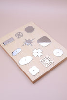 Eleven polished chrome cabinet knob backplates on a pale wooden board: round, oval, square, squircle, quatrefoil, pierced, fretwork, flower, star, oblong and rectangle