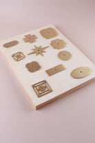 Eleven satin brass cabinet knob backplates on a pale wooden board: round, oval, square, squircle, quatrefoil, pierced, fretwork, flower, star, oblong and rectangle