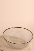 Thalia large clear glass bowl with a hammered texture and gold rim on a round wooden board